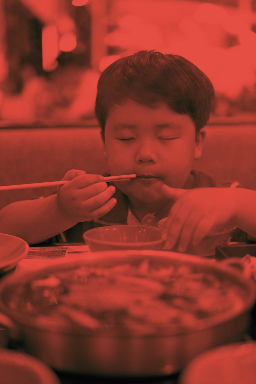 Một cậu bé ăn thịt bò luộc ngon lành với súp sukiyaki trong nồi shabu